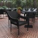 A black Flash Furniture Ethan synthetic rattan arm chair on a brick patio with a table and white plates.