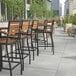 A row of Flash Furniture Lark Natural Faux Teak Slat Stackable Barstools with Arms on an outdoor patio.