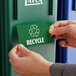 A person putting a Lavex Recycle Waste Stream label on a green recycle bin.