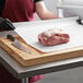 A person using Choice white freezer paper to cut and wrap a piece of meat on a cutting board.