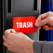 A person putting a red sign into a black trash can.