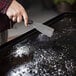 A hand using a Blackstone Griddle cleaning tool to scrape a black surface.