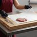 A person in an apron and gloves using Choice Freezer Paper to wrap meat on a cutting board.