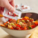 A hand pouring a TABASCO® Sriracha sauce packet into a bowl of food.