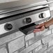 A hand pressing a button to open a Blackstone electric drop-in griddle with a hood.