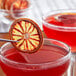 A dried blood orange slice on a stick in a glass of red liquid.