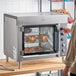 A man using a Vollrath electric countertop rotisserie oven with food inside.