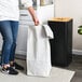 A woman removing a white liner bag from a black laundry hamper.