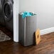 A stainless steel square laundry hamper with a wooden lid next to a washing machine.