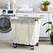 A Household Essentials commercial laundry cart with a black frame full of laundry in a laundry room.