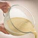 A person pouring liquid into a KitchenAid glass bowl.