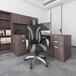 A Boss black and gray high-back office chair with padded arms next to a desk with binders on shelves.