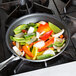 A Vollrath Wear-Ever aluminum non-stick fry pan filled with peppers and onions cooking on a stove.