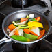 A Vollrath Wear-Ever non-stick fry pan filled with vegetables on a stove.