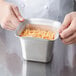 A person holding a Vollrath stainless steel food pan filled with noodles.