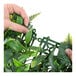 A person using a green plastic tool to hold a NatraHedge artificial rainforest living wall panel with green leaves.