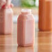 A person holding a clear customizable tall square juice bottle filled with pink liquid.