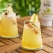 A pair of glasses of yellow liquid with pear slices on top.