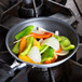 A Vollrath Wear-Ever aluminum non-stick fry pan filled with vegetables on a stove top.