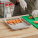 A person cutting carrots with a knife on a Vollrath stainless steel steam table pan.
