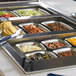 A Vollrath stainless steel rectangular food pan with food in it on a counter.