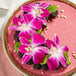 A pink cake with purple orchids on top.