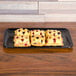 A Sabert Mozaik black plastic catering tray of pastries on a wood surface.
