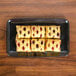 A Sabert Mozaik black plastic catering tray with a square pastry filled with fruit.
