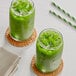 Two glasses of Tenzo matcha green liquid with ice and straws.