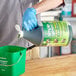 A person wearing blue gloves pouring green Simple Green liquid into a bucket.