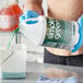 A person in blue gloves pouring Simple Green Sassafras Scented Concentrated Industrial Cleaner and Degreaser from a jug into a bucket.
