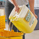 A woman pouring yellow Simple Green liquid into a yellow container.