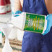 A person in blue gloves pouring Simple Green liquid into a white container with a green label.
