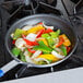 A Vollrath Wear-Ever aluminum non-stick fry pan filled with vegetables on a stove top.