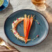 A Acopa Highlands skyfall blue coupe china plate with carrots and hummus on a table with a fork on a napkin.