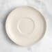 An Acopa Highlands white china saucer on a marble surface.