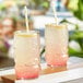 Two glasses of Tiki Breeze Clear Energy Shots with straws on a table.