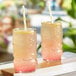A pair of clear glass tiki cups filled with a pink and yellow beverage, each with a straw.