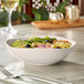 A bowl of salad with vegetables and nuts on a table.