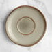 An Acopa Highlands heather gray saucer with a rim on a marble surface.