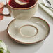 A hand holding a cup of tea with a Acopa Heather Gray saucer on a table