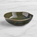 An Acopa Highlands juniper green china bowl on a white marble surface.