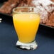 A glass of Anchor Hocking orange juice on a table.