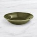 An Acopa Highlands juniper green bowl on a marble surface.