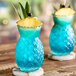 A blue drink in a Tiki glass with a pineapple garnish and a blue umbrella.