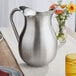 A Vollrath stainless steel water pitcher on a table.