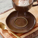A Acopa Highlands hazel china saucer with a cup of hot chocolate topped with whipped cream and sprinkles on a wooden table.