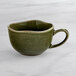 An Acopa Highlands juniper green china cup with a handle on a marble surface.