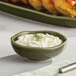 A round Acopa Juniper Green China sauce cup filled with white sauce and lemon wedges.
