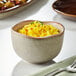 A close-up of a brown bowl filled with yellow rice with spices.